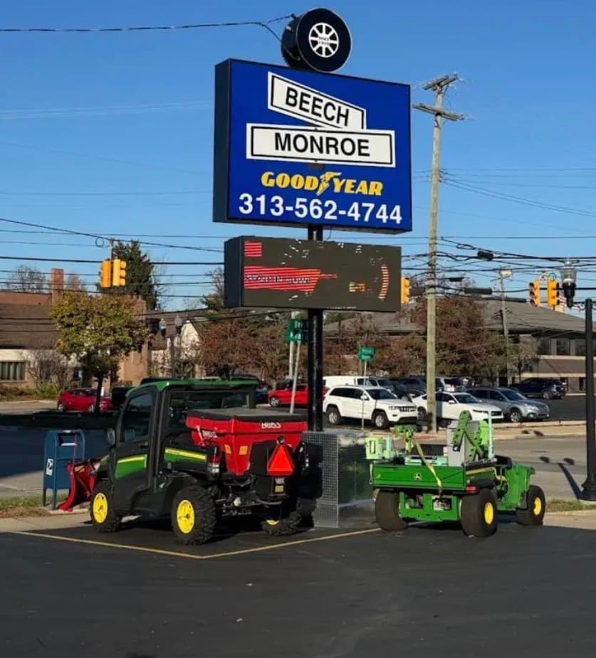Goodyear sign towers over two John Deere utility vehicles parked in a sunny lot.