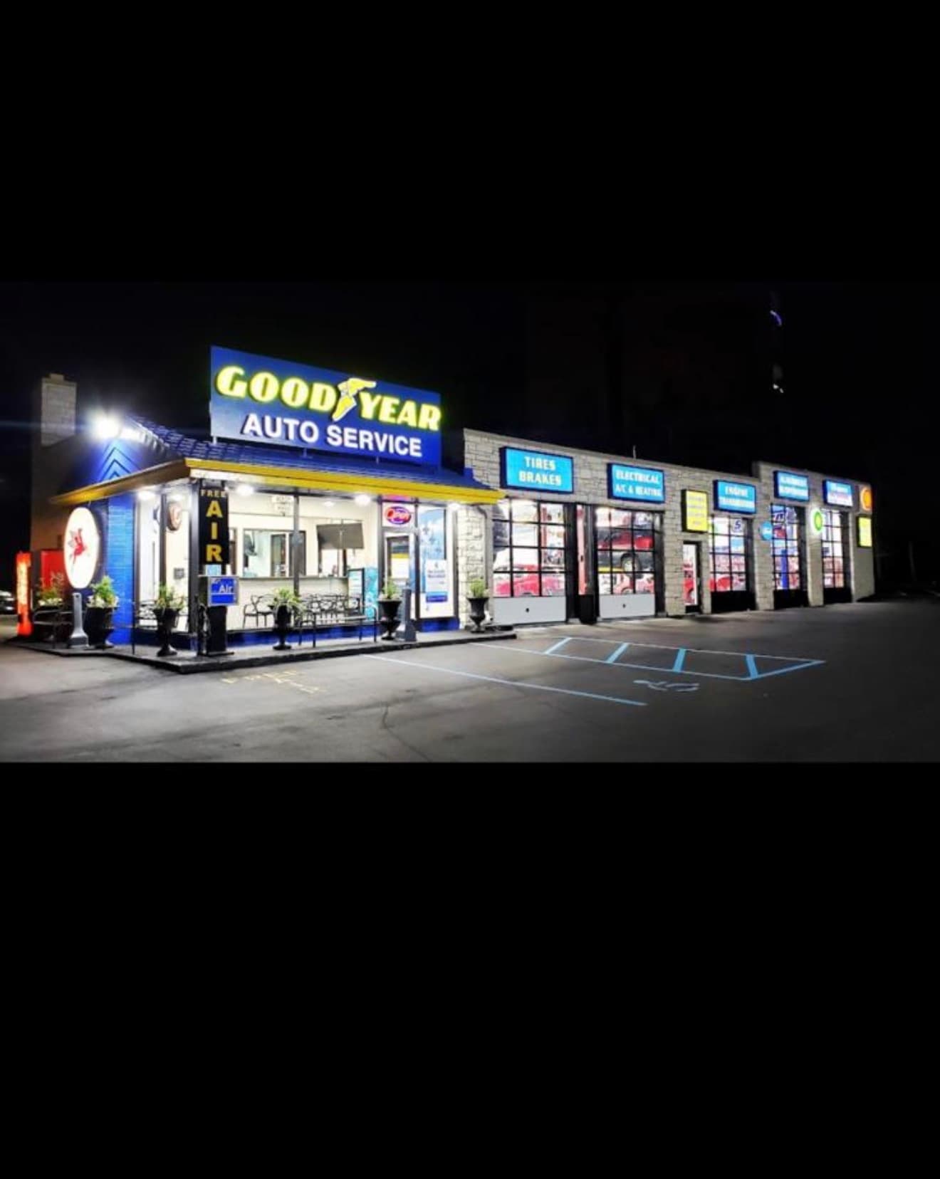 Goodyear Auto Service center at night with glowing blue signs and illuminated repair bays.